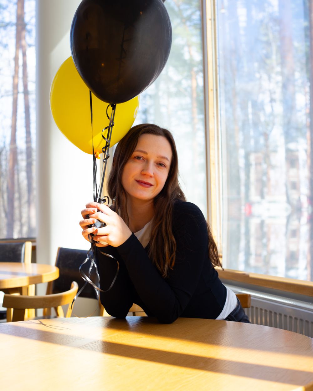 Laura Auna sitting at a café table holding yellow and black balloons
